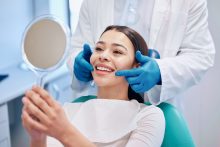 歯科医院で鏡で自分の歯並びを確認して笑う女性